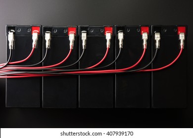 Rechargeable Batteries, And Electrical Wires. Industrial Battery Hooked Up In Parallel With Long Red And Black Cable Bundles, Coming From The Terminal. 