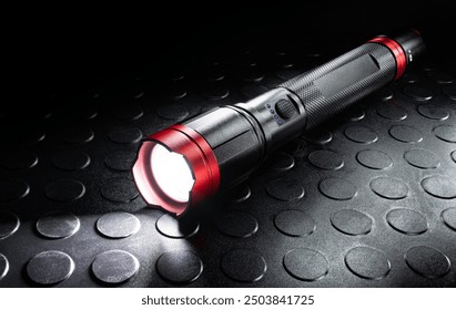 Rechargeable black and red metal flashlight with its LED activiated that is ideal for power outages, hurricanes of other natural disasters.