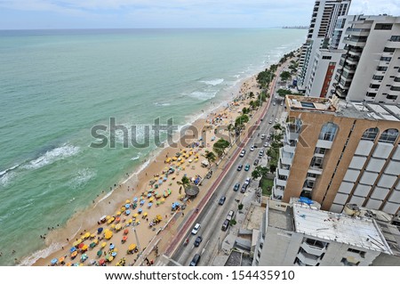 Recife, Pernambuco, Brazil, 2009. A view to the city beach with lots of Brazilian people sunbathing and swimming, and umbrellas, a view from the top of a skyscraper.