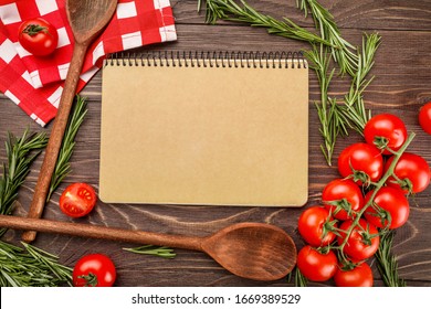 Recipe book, tomatoes, rosemary and wooden kitchenware on wooden background