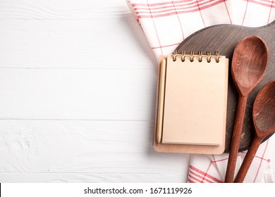 Recipe book, wooden spoons and board on white wooden background