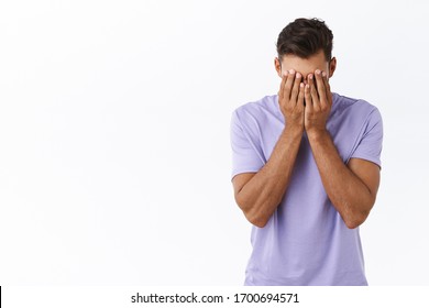 Reckless distressed, depressed young millennial guy in purple t-shirt, tired of problems, dont know how solve situation, cover face with hands, facepalm from fatigue and annoyance, white background