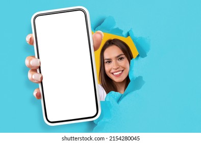 Recommendation. Happy Young Lady Holding Big Smartphone With Isolated White Screen In Hand, Showing Close To Camera Through Torn Blue Paper Hole. Gadget With Empty Free Space For Mock Up, Template