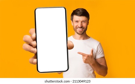 Recommendation. Portrait of excited bearded man holding big smartphone with white blank screen in hand, showing close to camera and pointing at device. Gadget with empty free space for mock up, banner