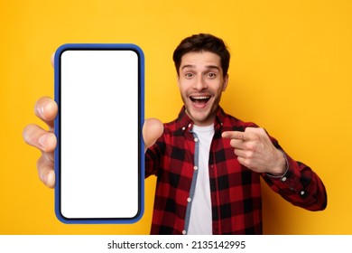 Recommendation. Portrait Of Excited Guy Holding Big Smartphone With White Blank Screen In Hand, Showing Close To Camera And Pointing At Device. Gadget With Empty Free Space For Mock Up, Yellow Banner