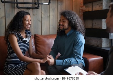 Reconciliation Of Spouses. Hopeful Young Black Family Couple Sitting On Couch At Counselor Office Looking In Each Other Eyes And Holding Hands Reconciling After Fight Giving Second Chance To Marriage