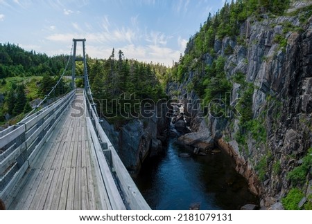 The reconstructed suspension bridge of the ghost town of La Manche, Newfoundland crosses over the cove beside a small waterfall, connecting the East Coast Trail.