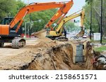 Reconstruction of the underground sewerage system on a city street in spring. Two excavators are digging a deep ditch. Traffic has been halted on a section of the street. Road works.