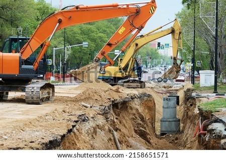 Reconstruction of the underground sewerage system on a city street in spring. Two excavators are digging a deep ditch. Traffic has been halted on a section of the street. Road works.