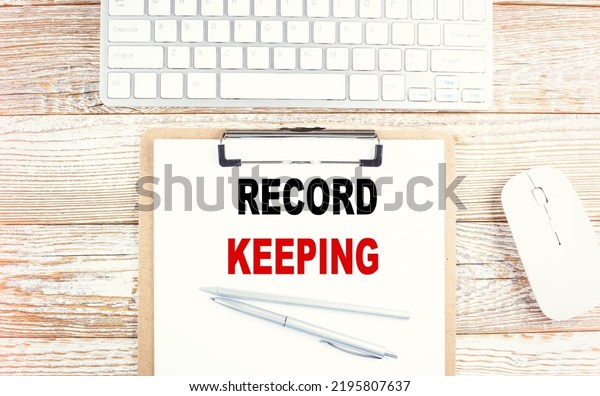 RECORD KEEPING text on clipboard with keyboard\
on wooden background