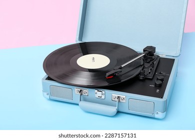 Record player with vinyl disk on table near pink wall