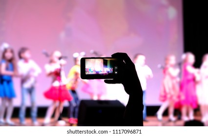 Record Video Or Photo Of Concert On Mobile Phone. Hand With Smartphone Records Live Kids Concert. Blurred Background.