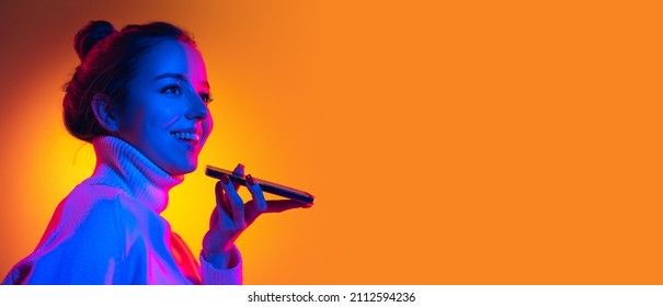 Record voice message. Flyer with young beautiful girl posing isolated on orange background in neon light, filter. Concept of emotions, facial expression, youth, aspiration, sales. Copy space for ad