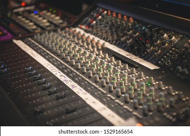 RECORDING STUDIO EQUIPMENT WITH KNOBS, METERS, FADERS AND BUTTONS, IMPRESSIVE DARK VENUE AND BLURRED BACKGROUND
