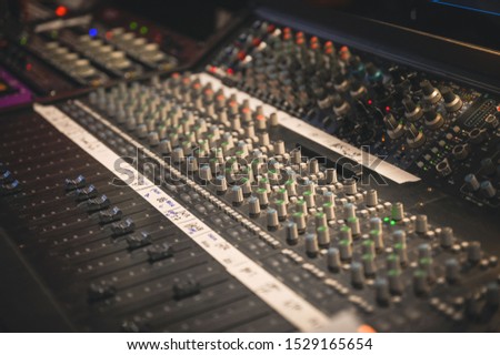 RECORDING STUDIO EQUIPMENT WITH KNOBS, METERS, FADERS AND BUTTONS, IMPRESSIVE DARK VENUE AND BLURRED BACKGROUND
