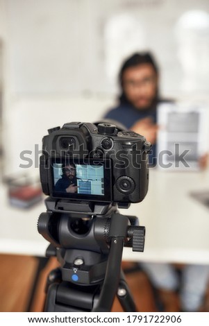 Recording video blog. Young man teaching online, explaining new theme while working from home. Focus on camera, professional digital equipment. E-learning. Distance education. Blogging, vlogging