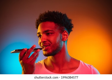 Recording voice message. African-american man's modern portrait on gradient orange studio background in neon. Beautiful afro model. Concept of human emotions, facial expression, sales, ad. - Powered by Shutterstock