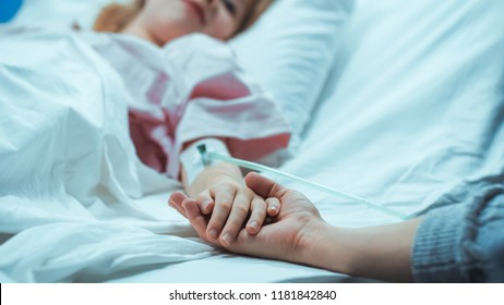 Recovering Little Child Lying in the Hospital Bed Sleeping, Her Hand Falls into Mother's and She Holds it Comfortingly. Focus on the Hands. Emotional Family Moment. - Powered by Shutterstock