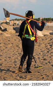 Recovering Man In Water Repellent Diving Suit Looking For Lost Metal Material During The Day With A Metal Detector On The Sandy Beach