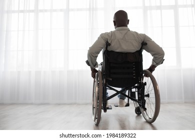 Recovery after injury or ill, self-isolation and new rules, lonely at home. Sad mature african american man disabled in wheelchair look at large window in clinic or living room interior, free space - Powered by Shutterstock