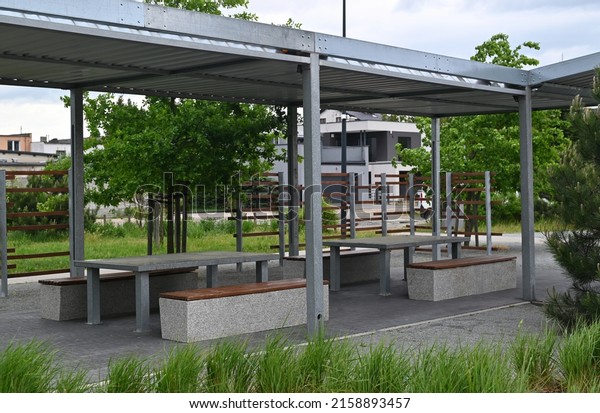 Recreation area with concrete\
tables and benches on a platform under a metal frame roof. play\
area, 