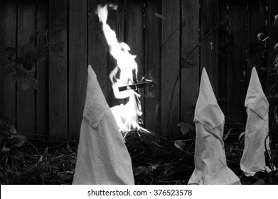 Recreation (fake) Ku Klux Klan members standing around and watching a burning cross outside and dusk.  KKK burning a cross. Hatred and bigotry concept. Black and white, photo reportage look and feel,