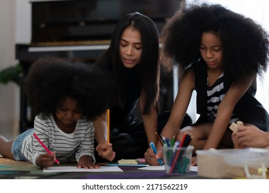 Recreational activities between mother and daughter, happy family painting together by using crayons and colored pencils at home to create imagination and develop muscles in living room.