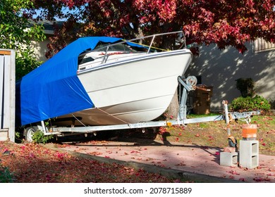 Recreational Boat On Trailer Stored On Driveway Of Residential Home. The Cruiser Is Covered With A Blue Tarp Tent For Protection.