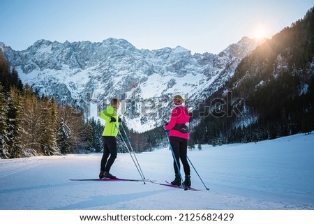 Recreational cross country mature skiers couple skiing on a sunlit snowy trail in nature with mountains.