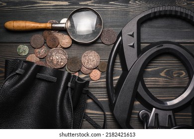 Recreational Metal Detector And Bag Full Of Ancient Coins On The Wooden Table Background. Treasure Hunting Concept Background.