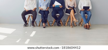 Recruitment process and office paperwork concepts. Low section crop of group of job candidates waiting in line for interview. Company workers with documents sitting in queue on chairs