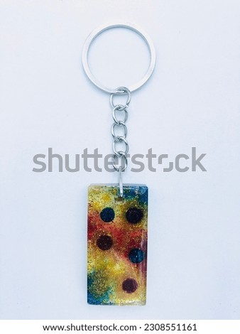 A rectangle shape keytag on white background. It has only blue yellow red colour glitter powder and it has silver colour keychain. It is made of resin material. It is really beautiful keytag. Love it.