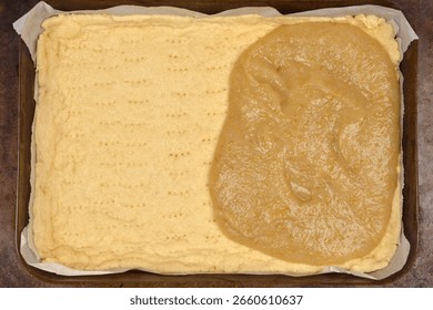 A rectangular baking pan with a partially baked pie crust, with cooked apple filling spread over approximately half of its surface