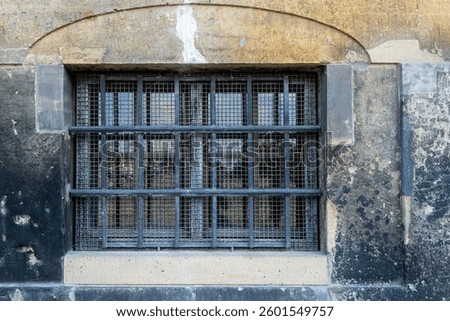 Rectangular basement window with iron grille and steel mesh against an old stone wall. From the series of windows of the world.