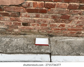 Rectangular box with red edges is positioned on cracked concrete sidewalk next to a brick wall, highlighting urban textures and surroundings
