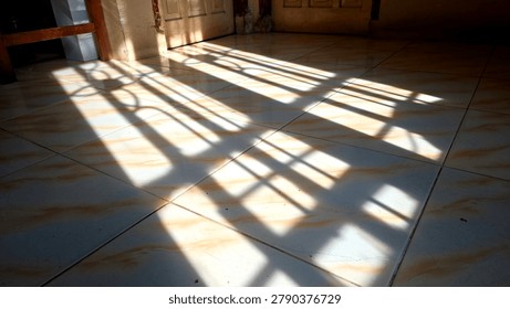 Rectangular ceramic floor tiles with dramatic sunlight shadows cast from a window onto the polished surface in a quiet room