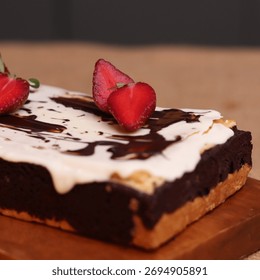 Rectangular chocolate brownie or cake with a thick white frosting layer, drizzled with chocolate sauce and topped with fresh strawberries, served on a rustic wooden board