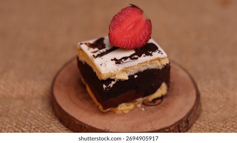 Rectangular chocolate brownie or cake with a thick white frosting layer, drizzled with chocolate sauce and topped with fresh strawberries, served on a rustic wooden board