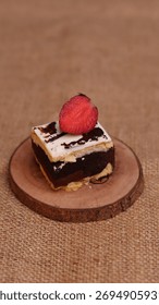 Rectangular chocolate brownie or cake with a thick white frosting layer, drizzled with chocolate sauce and topped with fresh strawberries, served on a rustic wooden board