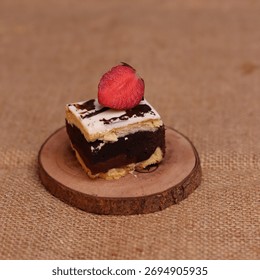 Rectangular chocolate brownie or cake with a thick white frosting layer, drizzled with chocolate sauce and topped with fresh strawberries, served on a rustic wooden board