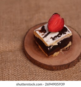 Rectangular chocolate brownie or cake with a thick white frosting layer, drizzled with chocolate sauce and topped with fresh strawberries, served on a rustic wooden board