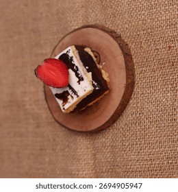 Rectangular chocolate brownie or cake with a thick white frosting layer, drizzled with chocolate sauce and topped with fresh strawberries, served on a rustic wooden board