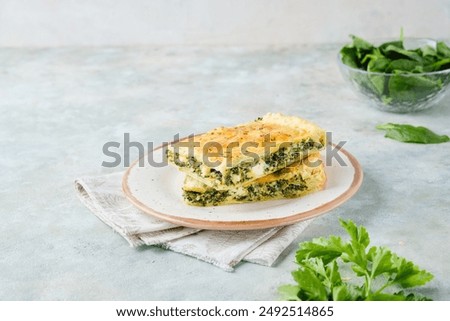 A rectangular chopped Greek pie with spinach and cheese on a plate on a gray concrete background. Spinach recipes. Greek cuisine