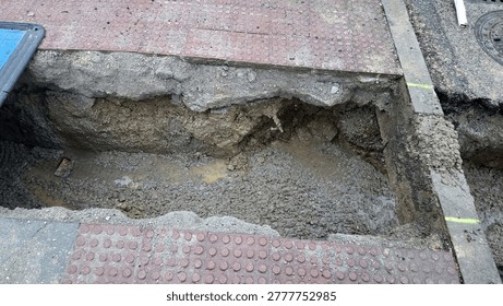 Rectangular excavated trench in sidewalk for drainage pipe installation and road repair background for infrastructure work signs.