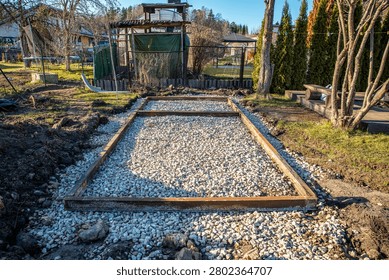 Rectangular foundation with rusted steel angles holds white crushed stone in a backyard workshop, late afternoon light casts long shadows on compacted aggregate.