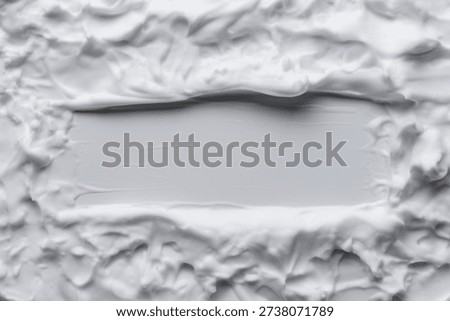 Rectangular frame carved into thick white shaving foam. Empty center space on white background surrounded by textured whipped cream or lather. Concept of cleanliness, hygiene, and copy space