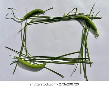  a rectangular frame made from three green pea pods placed at the top, bottom‑left, and bottom‑right corners, with thin green grass or chive stems arranged along all four sides to complete the border, set against a white background.