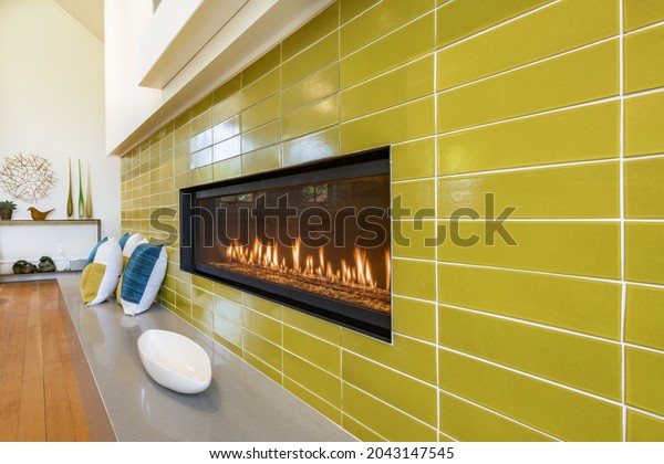 rectangular gas fireplace with chartreuse green\
tiles pillows flowers and steel art\
piece