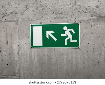 A rectangular green emergency exit sign with white pictograms mounted on a textured concrete wall.