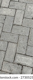 Rectangular grey concrete paving blocks are arranged in a herringbone pattern on a pedestrian walkway to create a durable and stable surface.